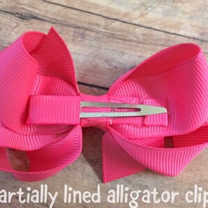 Pu&ograve; includere: Un fiocco rosa con una clip per alligatore parzialmente foderata.