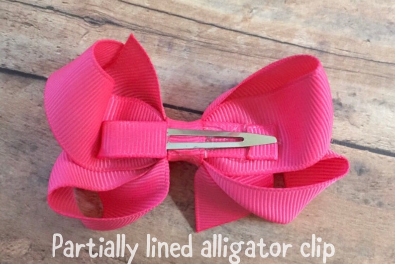 Pu&ograve; includere: Un fiocco rosa con una clip per alligatore parzialmente foderata.
