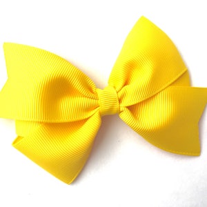Pode incluir: Um la&ccedil;o amarelo brilhante feito de fita de grosgrain. O la&ccedil;o &eacute; amarrado com um n&oacute; simples e tem uma textura ligeiramente enrugada.