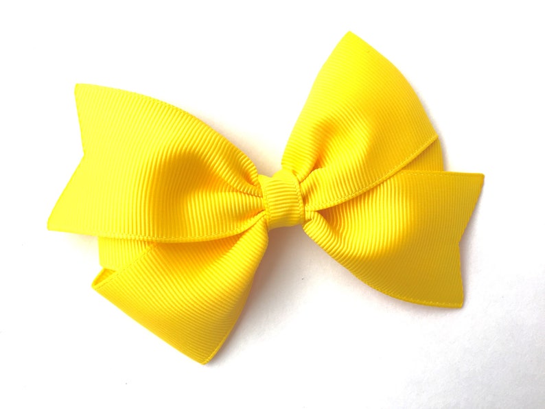 Pode incluir: Um la&ccedil;o amarelo brilhante feito de fita de grosgrain. O la&ccedil;o &eacute; amarrado com um n&oacute; simples e tem uma textura ligeiramente enrugada.