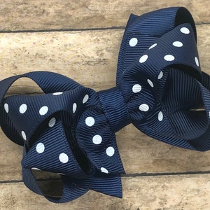 May include: A navy blue hair bow with white polka dots. The bow is made of grosgrain ribbon and has a classic, layered design. This accessory is suitable for various occasions and adds a touch of charm.