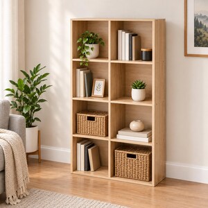 May include: A light wood-toned bookshelf featuring eight rectangular cubby compartments. The shelves are organized with various items including books, two woven storage baskets, a small framed picture, a white ceramic pot, and a small plant.