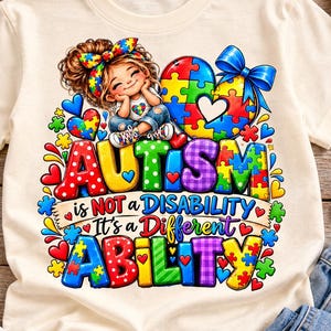 Puede incluir: Una camiseta de color crema con un gráfico de un niño con un lazo de piezas de rompecabezas de colores, un gran corazón de piezas de rompecabezas y el texto: "AUTISM is NOT a DISABILITY It's a Different ABILITY." El diseño incluye varios corazones y piezas de rompecabezas de colores.