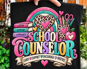 May include: A black t-shirt featuring a colorful graphic with a rainbow, a leopard print heart, a stack of books labeled LISTEN, SUPPORT, EMPOWER, a pencil cup, an apple, and the text SCHOOL COUNSELOR with GUIDE, SUPPORT, ENCOURAGE, INSPIRE.