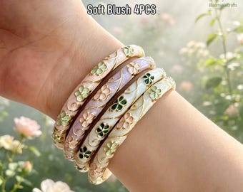 May include: A set of four bangles featuring gold-tone metal vines and enamel flower accents in shades of pink, green, and white. The bracelets are labelled Soft Blush 4PCS and display a delicate floral pattern with smooth, rounded edges.