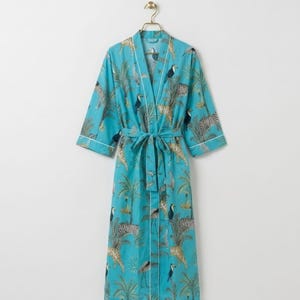 May include: A turquoise robe featuring a repeating pattern of zebras, toucans, and palm trees. The garment has three-quarter length sleeves, a tie-waist belt, and white piping along the front opening, collar, and sleeve cuffs, hanging on a hanger.
