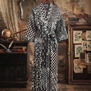 May include: A long-sleeved robe featuring a patchwork design in black, white, and gray. The garment displays various patterns including polka dots, swirling circles, and botanical motifs. It includes a matching tie belt at the waist and a shawl collar.