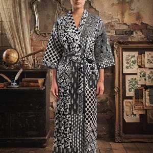May include: A long-sleeved robe featuring a patchwork design of black and white patterns, including polka dots, floral motifs, and geometric shapes. The garment has a shawl collar, a tie-waist belt, and a calf-length hemline with a straight silhouette.