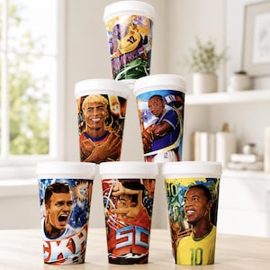 May include: A stack of six white plastic cups featuring colorful graphic illustrations of various soccer players in action. Each cup displays a unique athlete portrait, dynamic sports scenes, and bold text elements, arranged in a pyramid formation.