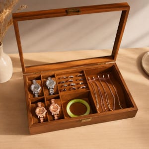 May include: A rectangular wooden jewelry storage box with a clear glass lid and a brown velvet interior. The box features four watch compartments, a ring section, a circular bangle holder, and a side area for necklaces, all lined in brown fabric.