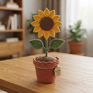 Peut inclure: Un tournesol au crochet avec des pétales jaune vif et un centre marron foncé, fixé sur une tige verte avec deux feuilles. La fleur est plantée dans un pot au crochet couleur terre cuite avec un bord festonné et une étiquette Handmade with Love.
