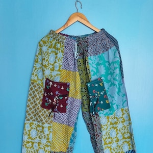 Puede incluir: Pantalones de patchwork con cintura elástica y cordón, dos bolsillos delanteros con cierre de lazo y una variedad de estampados florales, de cachemira y de chevrón en tonos verde, amarillo, azul, morado y granate en la tela.