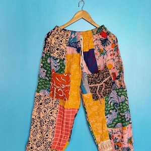 Puede incluir: Pantalones de patchwork con una vibrante mezcla de cuadrados de tela multicolor con diversos estampados florales, geométricos y de animales. Los pantalones tienen una cintura elástica con cordón blanco, dos bolsillos delanteros y bajos ajustados.