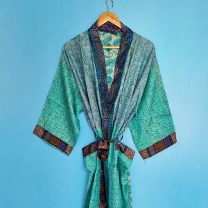 Könnte beinhalten: Ein leichter Morgenmantel im Kimono-Stil mit einer leuchtend türkisen und blaugrünen Basis sowie aufwendigen dunkelblauen und braunen Musterrändern an Kragen, Ärmelbündchen und Bindegürtel. Das Kleidungsstück hat weite Ärmel und einen passenden Stoffgürtel.