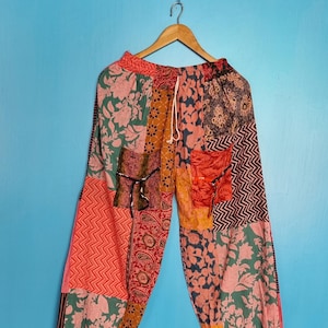 Könnte beinhalten: Patchwork-Hose mit einer Vielzahl bunter Stoffbahnen mit Blumen-, Paisley- und Zickzackmustern in Orange-, Rosa-, Grün- und Schwarztönen. Die Hose hat einen elastischen Bund mit weißem Kordelzug sowie elastische Beinabschlüsse.