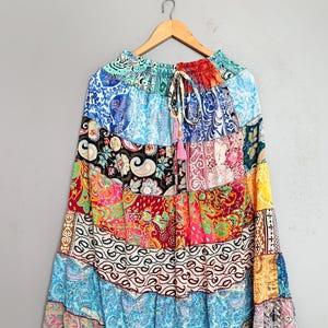May include: A tiered maxi skirt featuring a vibrant patchwork of multicolored fabrics with intricate paisley and floral patterns. The skirt has an elasticized waistband with a drawstring tie and a flowing, flared silhouette with multiple horizontal panels.
