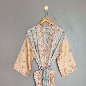 Puede incluir: Una bata de manga larga con un diseño de patchwork de varios patrones florales en tonos melocotón, azul claro y blanco. La prenda incluye un cinturón de tela a juego en la cintura y mangas anchas, confeccionada con múltiples paneles de tela.