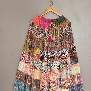 May include: A long, tiered skirt featuring a patchwork design with various colorful patterns, including floral, paisley, and geometric prints in shades of pink, blue, yellow, and white. The skirt has an elasticized waistband with a drawstring tie.