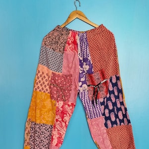Puede incluir: Pantalones de patchwork con una variedad de paneles de tela coloridos con patrones florales, de cachemira y de rayas en tonos rosa, naranja, amarillo, morado y azul. Los pantalones tienen una cintura elástica con cordón y puños elásticos.