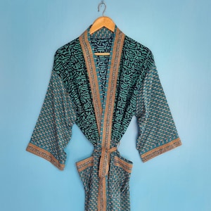 May include: A long-sleeved robe featuring a teal and black patterned fabric with a contrasting orange and blue border along the front opening, collar, and cuffs. The garment includes a matching fabric tie belt and two front pockets.