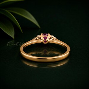 May include: A gold ring featuring a central round-cut pink gemstone held in a prong setting, flanked by two smaller clear stones on each side. The band is smooth and polished, showcasing a classic design with a refined metal finish.