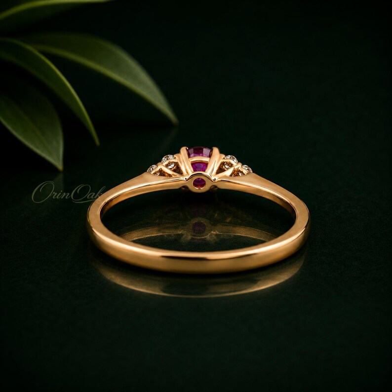 May include: A gold ring featuring a central round-cut pink gemstone held in a prong setting, flanked by two smaller clear stones on each side. The band is smooth and polished, showcasing a classic design with a refined metal finish.