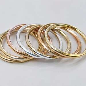 May include: A set of seven smooth, round metal bangles arranged in a slightly overlapping stack. The collection features a mix of polished yellow gold, rose gold, and silver-toned finishes, each with a simple, unadorned, and circular band design.