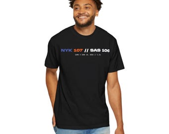May include: A black short-sleeve t-shirt featuring the text NYK 107 // SAS 106 in blue, orange, and white, with the smaller text GAME 4 JUNE 10, 2026 // 1.2s printed underneath. The shirt has a crew neckline and a standard fit design.