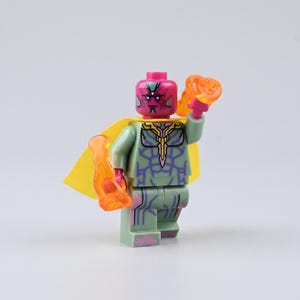 Puede incluir: Una minifigura de plástico con cabeza magenta, torso y piernas de color verde claro con patrones púrpuras similares a circuitos, una capa amarilla y accesorios translúcidos de color naranja en forma de llama en cada mano.