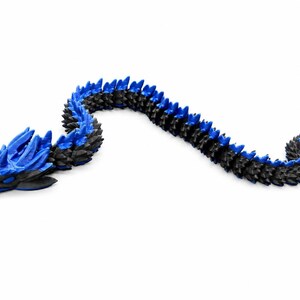 May include: A flexible, articulated dragon figurine featuring a black body with vibrant blue spikes along its back and head. The creature has a segmented, serpentine design with a detailed head, pointed horns, and a tail, all rendered in a two-tone colour scheme.