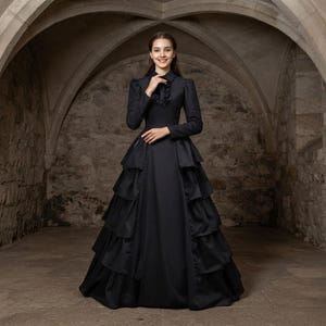 May include: A floor-length black dress featuring long sleeves, a high collar with a ruffled neckline, and a button-down front. The skirt is designed with multiple horizontal tiered layers of fabric that create a voluminous, structured silhouette.