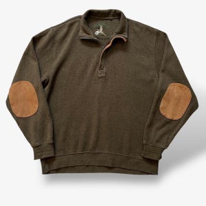 May include: An olive green quarter-zip pullover jumper featuring a stand-up collar, long sleeves with tan suede elbow patches, and the Orvis brand logo embroidered in green and white on the inner neck label area.