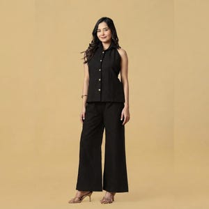 Peut inclure: Un ensemble noir composé d'une chemise sans manches à col pointu avec une patte de boutonnage frontale et d'un pantalon large assorti. La chemise présente une rangée de boutons clairs sur le devant, complétée par un pantalon ample en tissu noir.