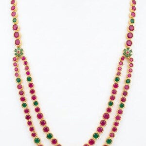 Peut inclure: Un long collier en or au design à double rangée, composé de pierres rondes serties clos alternant entre le magenta et le vert. Les deux rangées se rejoignent sur des motifs floraux de chaque côté, formant un seul rang vers le haut.