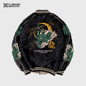 May include: A black bomber jacket featuring a large embroidered green dragon head, a yellow crescent moon, and lightning bolts on the back. The text X-URBAND ABSOLUTE RAIJŪ DRAGON is printed below the dragon. Sleeves feature green dragon embroidery.