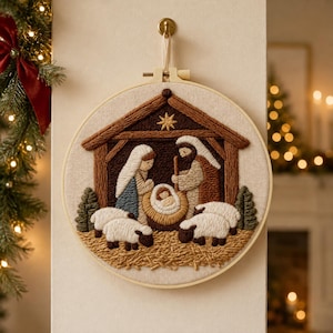 Peut inclure: Une décoration murale circulaire en tambour à broder représentant une scène de nativité en punch needle texturé. Le motif montre une étable avec une étoile, des personnages en robes bleue et marron, un nourrisson et quatre moutons blancs.