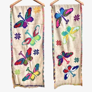 Puede incluir: Dos tapices de pared de tela beige con mariposas bordadas de colores. Las mariposas son de varios colores, incluyendo rojo, verde, azul, amarillo y rosa.