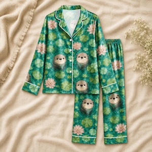 Può includere: Un set da pigiama composto da una camicia a maniche lunghe con bottoni e pantaloni abbinati in verde scuro. Il tessuto presenta un motivo ripetuto di lontre marroni, fiori di loto rosa e ninfee verdi con profili bianchi sul colletto.