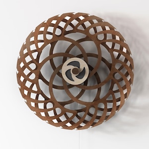 Puede incluir: Una escultura de pared circular con un complejo patrón de celosía entrelazada hecho de madera marrón. El diseño consta de segmentos curvos y repetitivos que irradian desde un disco central de madera clara con una incrustación circular gris oscuro.