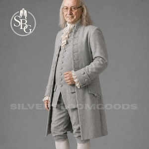 May include: A light gray long-sleeved coat and matching knee-length breeches featuring a button-down front, a white ruffled cravat, and white ruffled cuffs. The garment set is displayed with the text SILVERBLOOMGOODS and a circular logo.