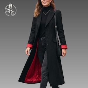 May include: A long black coat featuring a vibrant red interior lining and red cuffs. The coat has a structured collar, a button-front closure, and long sleeves. It is worn over a black turtleneck sweater and dark grey jeans, with a black shoulder bag.