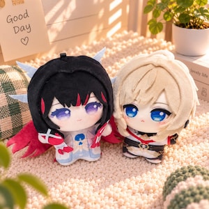 May include: Two plush dolls featuring anime-style designs. The left doll has black hair with red highlights, purple eyes, and red wing-like accents. The right doll has blonde hair, blue eyes, and a white and black outfit with red details.