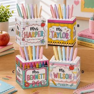 Peut inclure: Quatre porte-crayons carrés avec des motifs colorés et des noms personnalisés. Le modèle A présente des motifs de papier ligné, le B des crayons jaunes, le C des crayons de cire et le D des rayures pastel. Chaque pot contient cinq stylos.