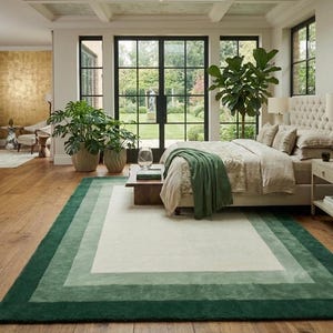 May include: A rectangular area rug featuring a layered border design with a large cream-colored center panel framed by concentric bands of light sage green and deep forest green, all set against a natural wood floor in a bedroom setting.
