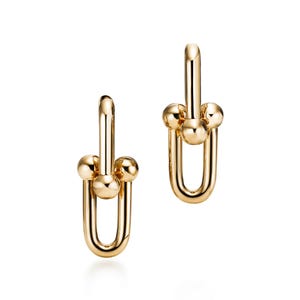 Peut inclure: Une paire de boucles d'oreilles en métal doré poli présentant un design en forme de maillon en U vertical. Chaque boucle se compose d'une boucle ovale allongée et lisse reliée à une barre horizontale avec une bille sphérique à chaque extrémité.