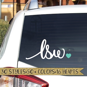 May include: White vinyl car decal with the word "love" written in cursive with a teal heart. The decal is on the back window of a white car. The text "30 STYLES. 50+ COLORS. 16 HEARTS" is below the decal.