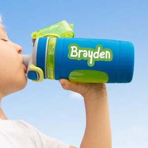 Pu&ograve; includere: Una bottiglia d'acqua blu e verde con un tappo verde e un adesivo bianco che dice "Brayden".