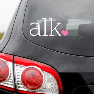 May include: A black car with a white vinyl sticker that says "alk" with a pink heart.