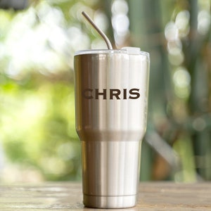 May include: A stainless steel tumbler with a straw and the name "CHRIS" engraved on the side.