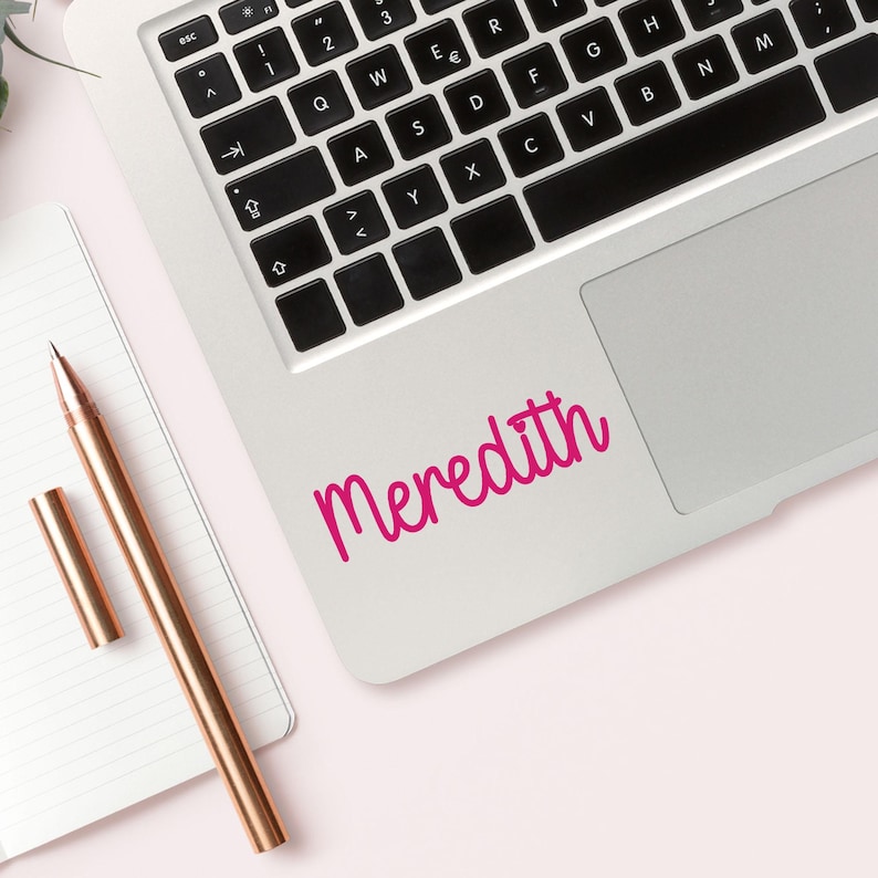 May include: A silver laptop computer with a pink vinyl sticker that says "Meredith" on the top right corner of the laptop.